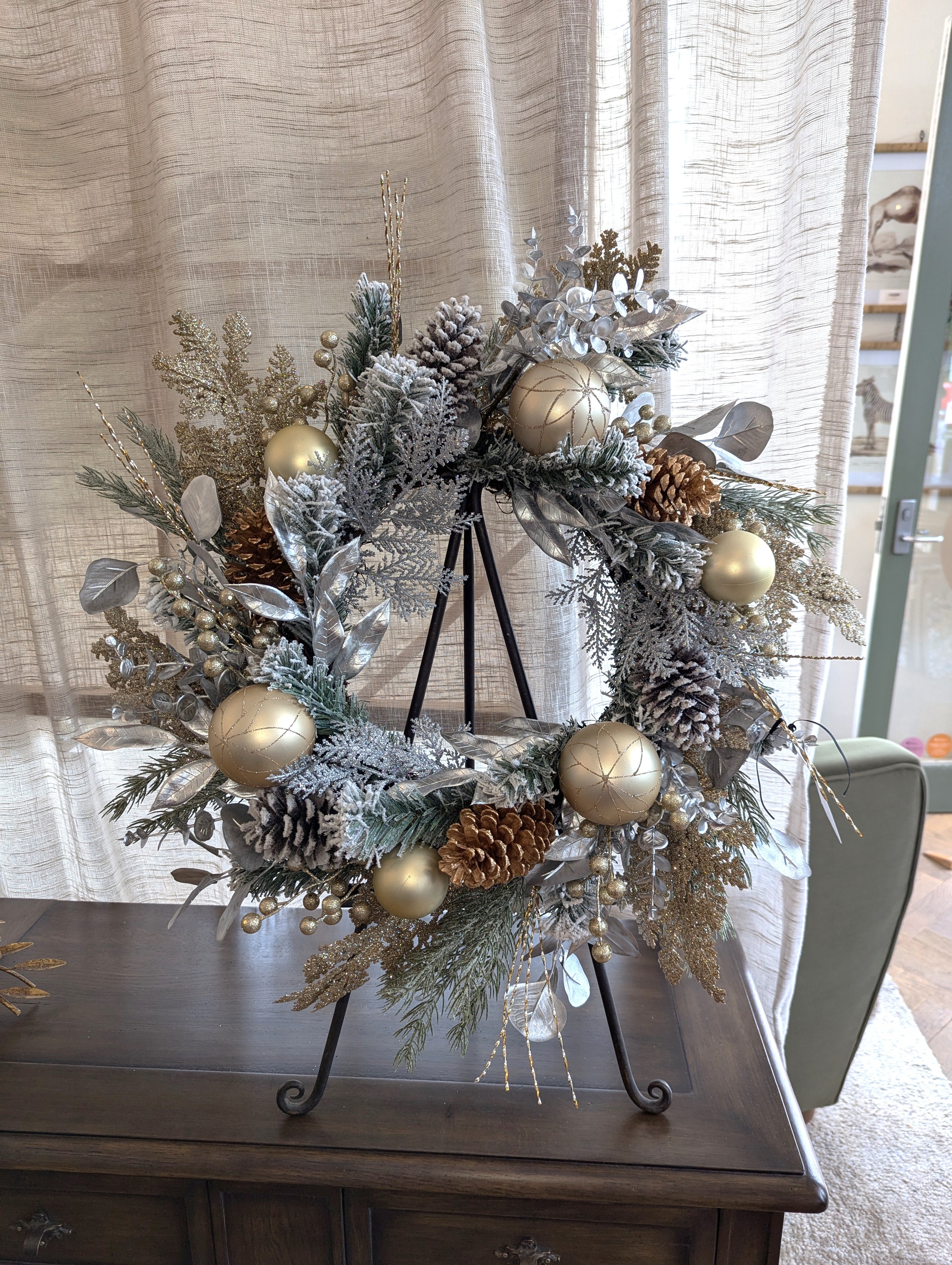 CHristmas wreath with silver and gold accents, baubles and pine cones on green foliage.